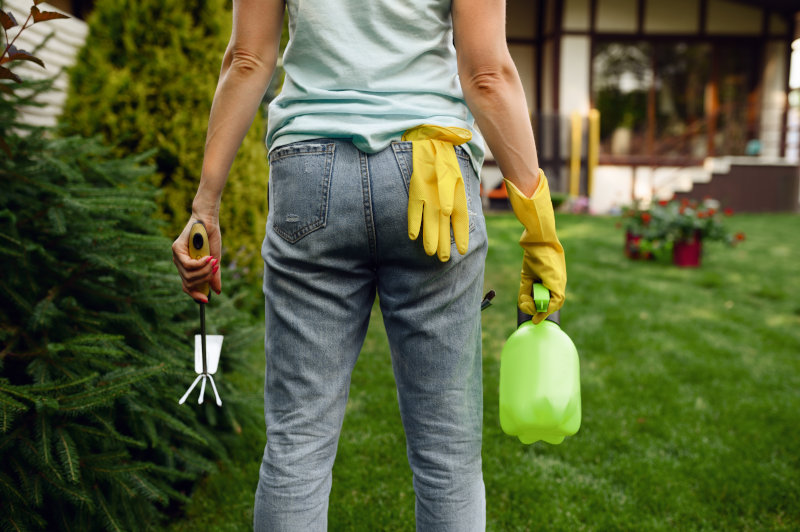 Frau mit Moosentferner in einer Sprühflasche und Schutzhandschuhen.
