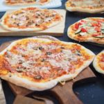 Mehrere Pizzen auf Pizzasteinen und eine Pizza auf einem Pizzaschieber